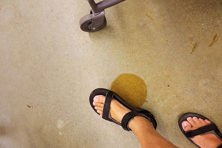 Small spill of liquid on a floor, foot with black sandal hovering over liquid
